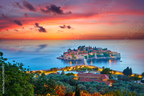 Amaizing sunset view on Sveti Stefan Island City. Small islet and resort in Montenegro. Balkans, Adriatic sea, Europe. Dramatic red sky under a Saint Stefan peninsula.