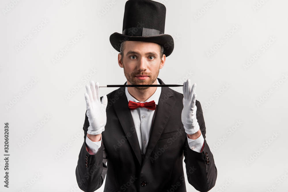 young magician in suit and hat holding wand, isolated on grey young magician in suit and hat holding wand, isolated on grey
