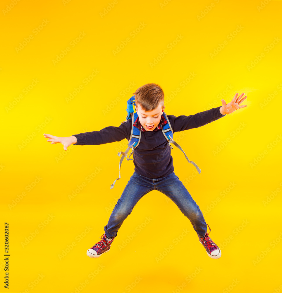 Happy kid jump with hand up. Cute exciting child boy ready to study with backpack isolated on yellow