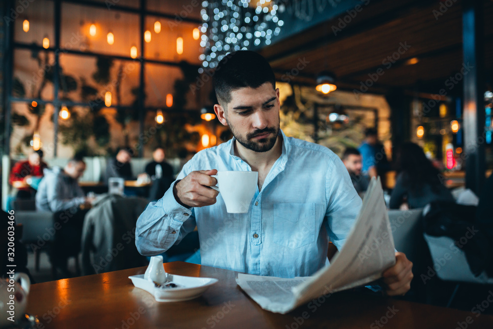 young man drinking tea and reading newspapers in cafeteria