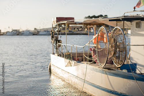 A moored fishing boat is waiting to set sail water while the sun reflects on the sea early in the morning with the winch of the fishing net in the foreground