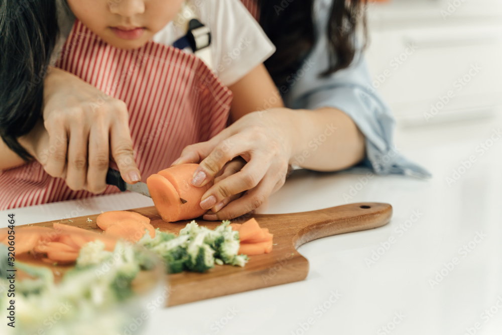 Young asian family cooking food in kitchen.Cute little girl and her beautiful parents are cutting vegetables and smiling while cooking in kitchen at home.Happy family in the kitchen concept.