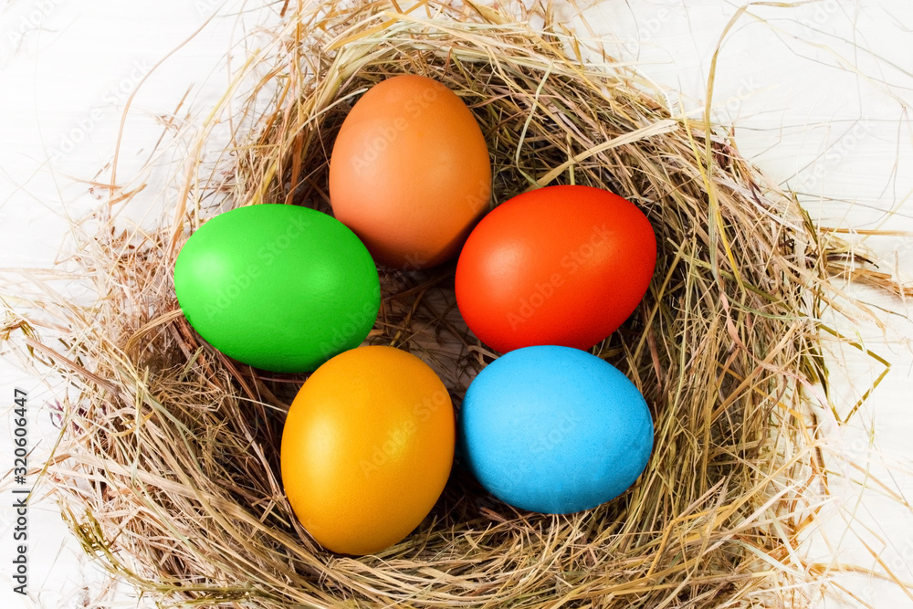 Five Easter eggs painted with multi-colored paints lie in the shape of a flower in a nest of dry grass on a white background close-up. Five Easter eggs painted with multi-colored paints lie in the shape of a flower in a nest of dry grass on a white background close-up.