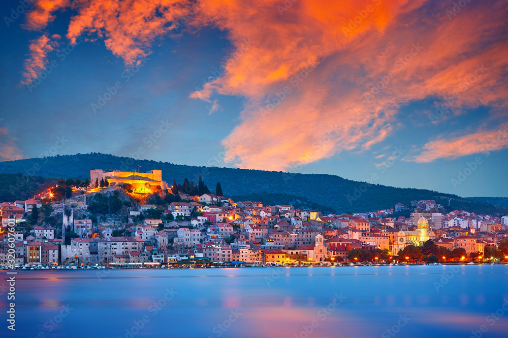 Fototapeta premium Large panorama of Unesco heritage historic town of Sibenik on Adriatic sea, Dalmatia, Croatia. Shot from the sea, harbor, waterfront and cathedral in front. Dramatic red sky at night..