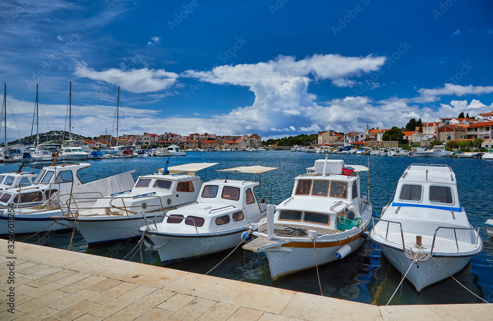 Fototapeta premium Fishing and sailing boats at the harbor. Sunny summer view of Tribunj port. Morning seascape, Adriatic sea, Croatia, Europe. Beautiful world of Mediterranean countries. Traveling concept background..