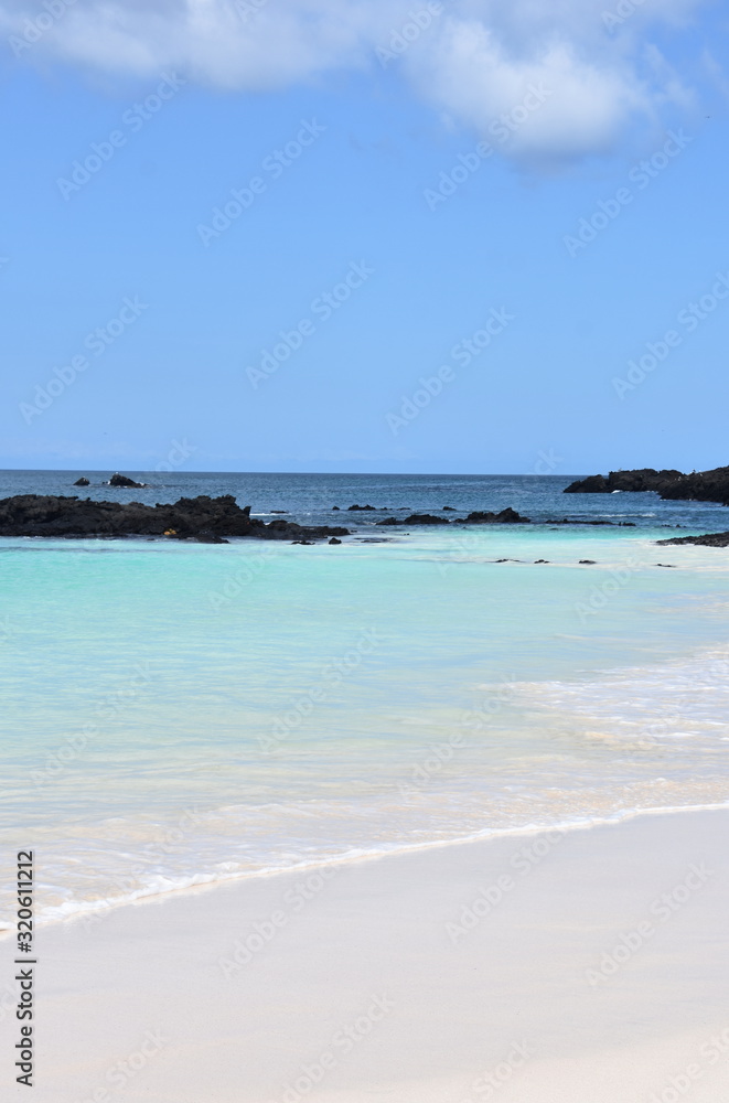 Sandy tropical beach and blue turquoise ocean water under blue sky and lava stones