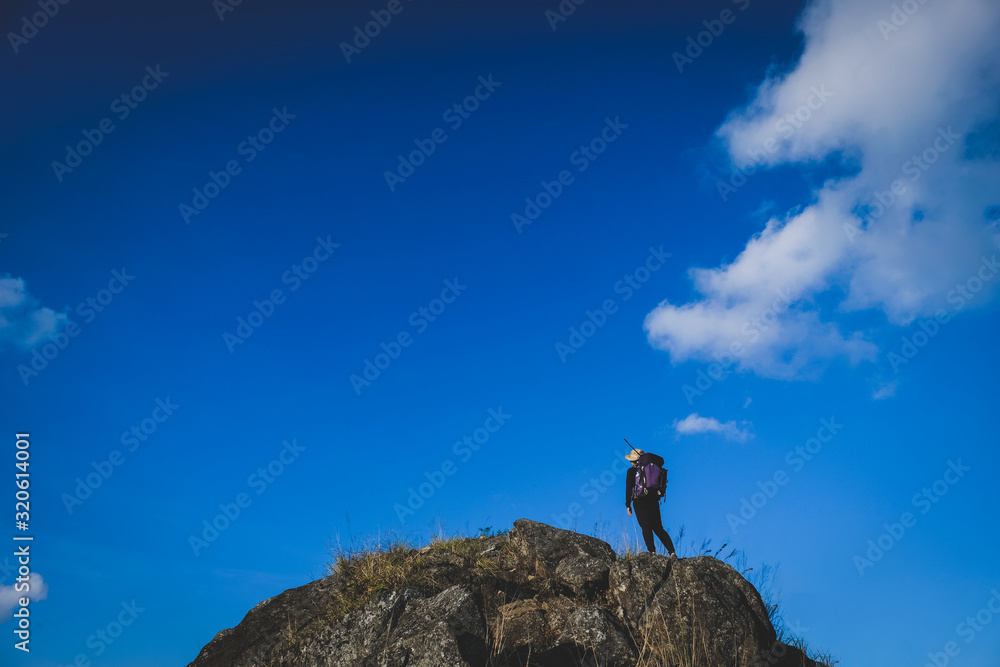 Hiker woman on the rock cliff against the clearly blue sky and cloud
