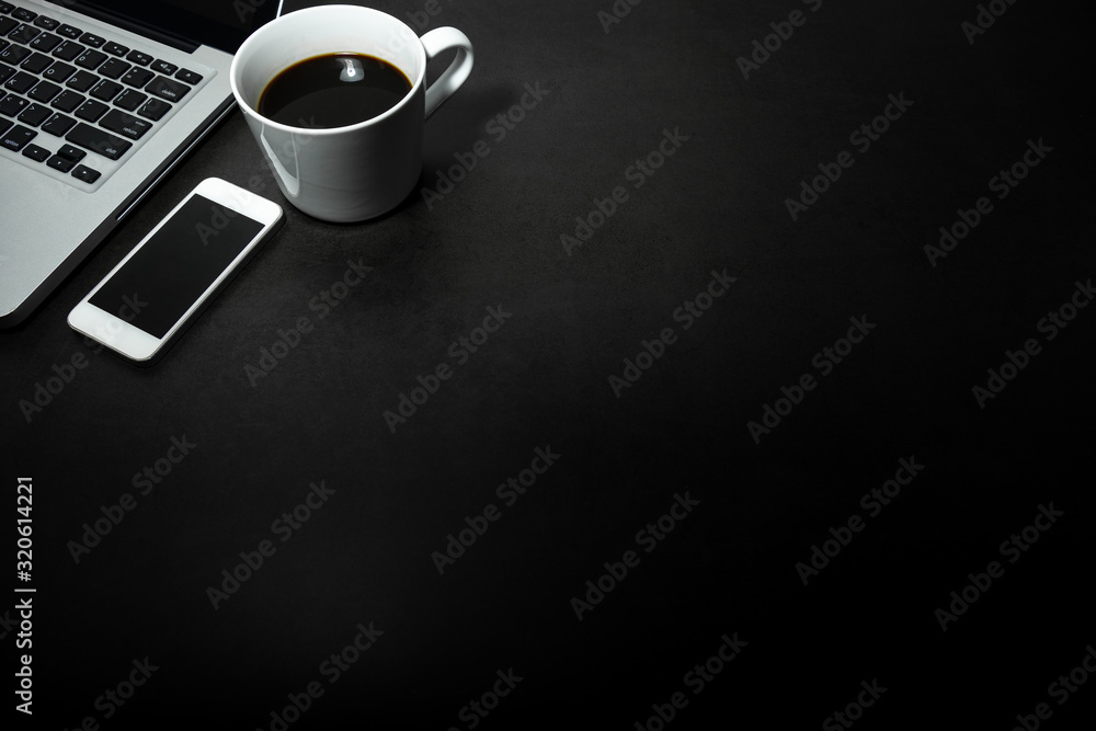 Fototapeta Laptop, biały telefon komórkowy i filiżanka czarnej kawy na pustym ciemnym tle, motyw biura roboczego