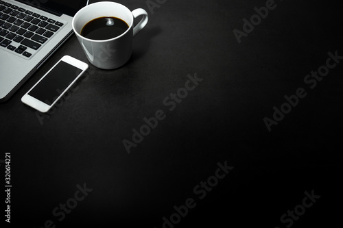 Laptop, white mobile phone  and a cup of black coffee against empty dark background, working office theme