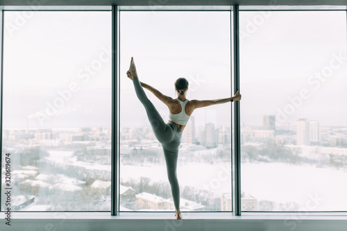Stretching in the white room by the window. Beautiful girl athlete on the Mat. Flexibility exercises on a light background.