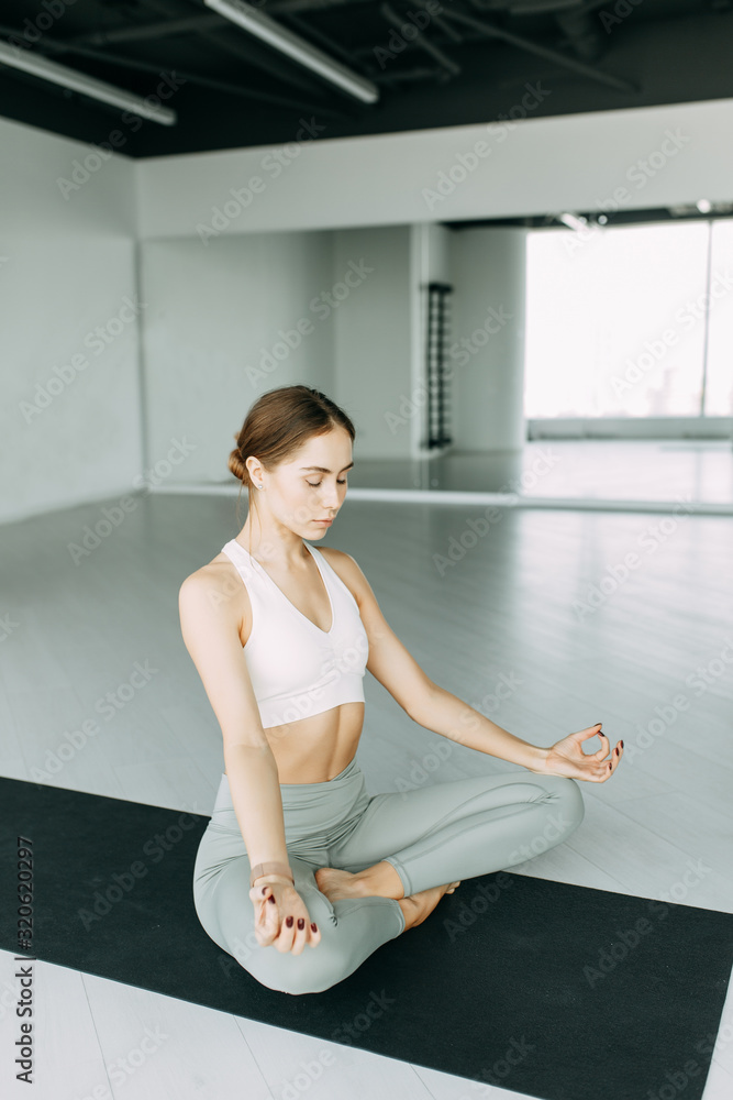  Exercises for self-control in yoga. Bright gym. Relaxed posture during meditation. The girl is sitting on the Mat, relax.