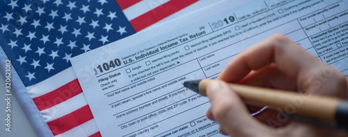 Form 1040 U.S. Individual  Income Tax return and hand with pen on flag of USA background. Wide photo. Close up view. photo