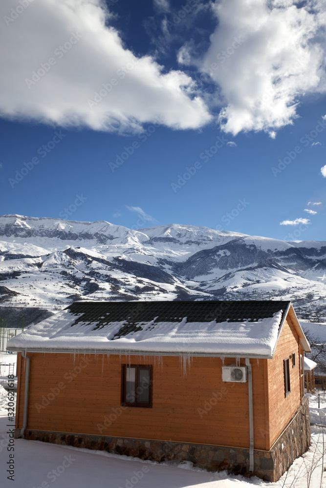 Small wooden houses at snowy winter mountains and blue sky with clouds