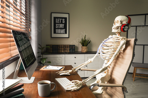 Human skeleton with headphones using computer at workplace photo