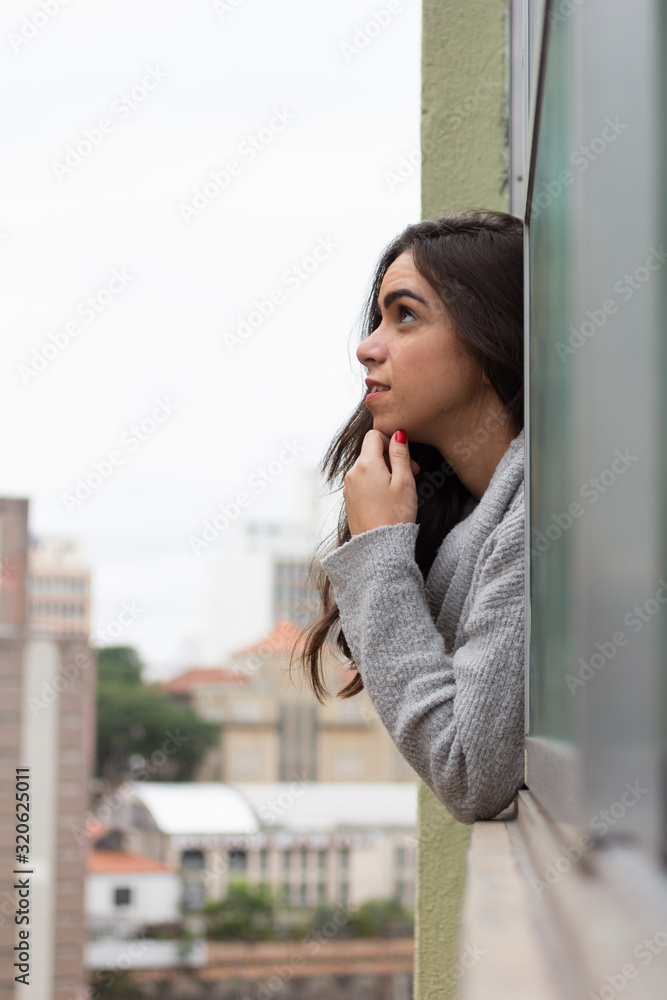 Young woman looking out the window at Sao Paulo city. Thoughts about the future, emotions, planning and tranquility. Buildings in urban scene.