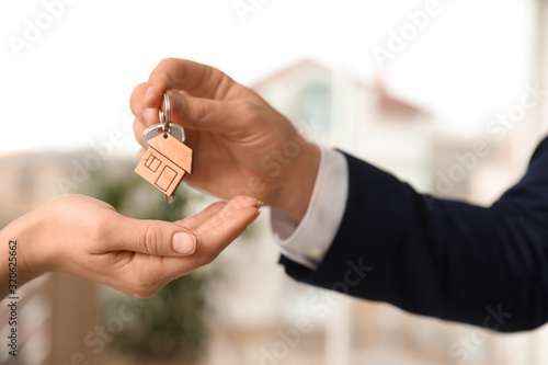 Real estate agent giving key with trinket to client in office, closeup