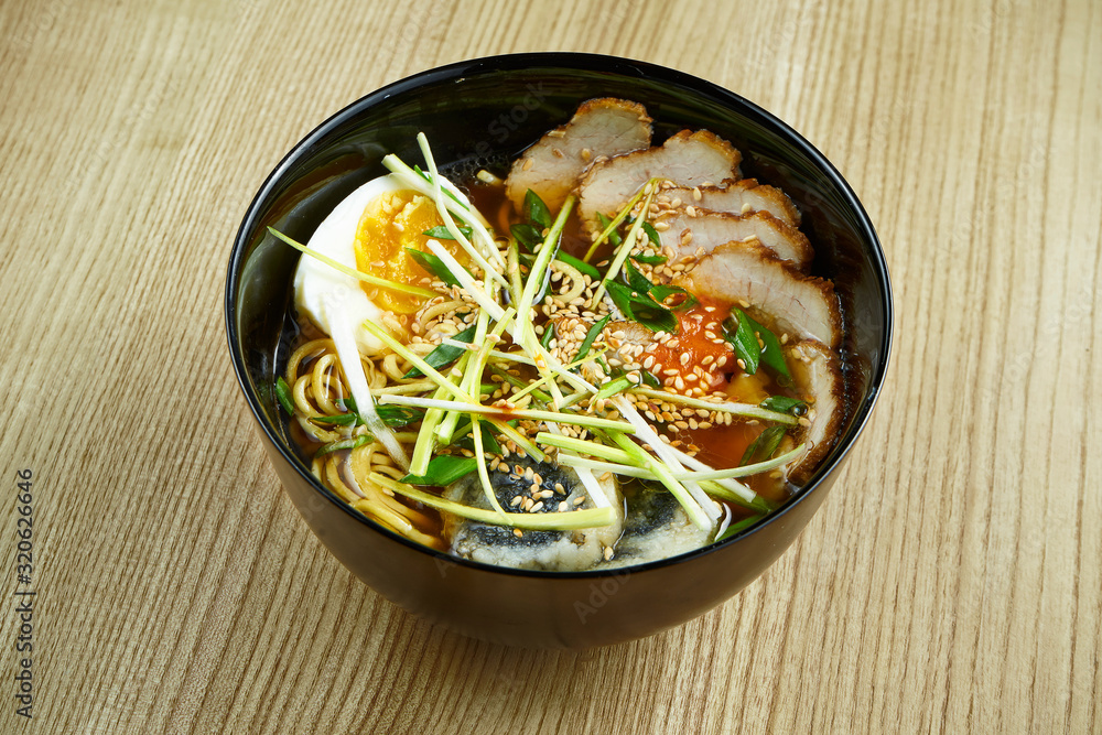 Traditional thai ramen soup with noodles, meat, shiitake mushrooms and egg in a black bowl on a wooden background. Delicious food close up Traditional thai ramen soup with noodles, meat, shiitake mushrooms and egg in a black bowl on a wooden background. Delicious food close up