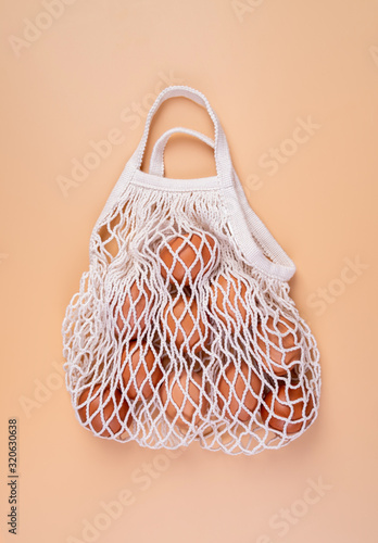 Eggs in a white shopping net bag isolated on beige background top view flat lay