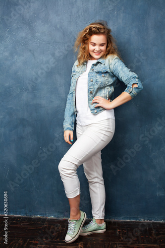 young pretty hipster girl with curly blond hair posing emotonal on blue wall background, lifestyle people concept