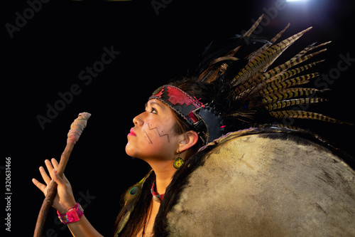 close up of young woman Teotihuacana, Xicalanca - Toltec in black background, with traditional dress dance with a trappings with feathers and drum photo