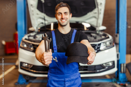 Fototapet focus on auto technician hands holding wrenches and cap with car on the backgrou