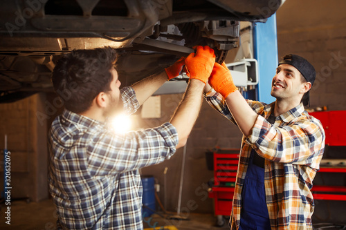 Two young automechanics working on a car in a repair workshop, sun effect photo