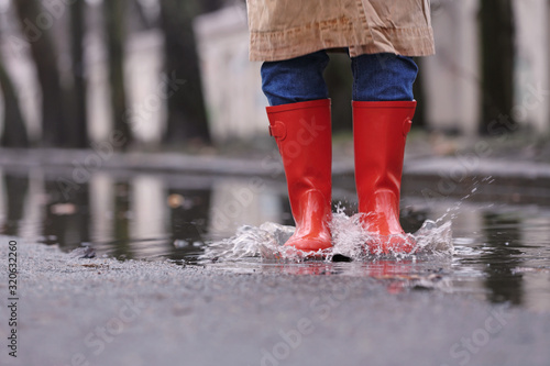 Woman in rubber boots jumping over puddle on rainy day, closeup. Space for text