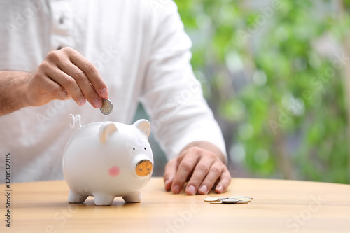 Cuadro en lienzo Man putting money into piggy bank at table, closeup