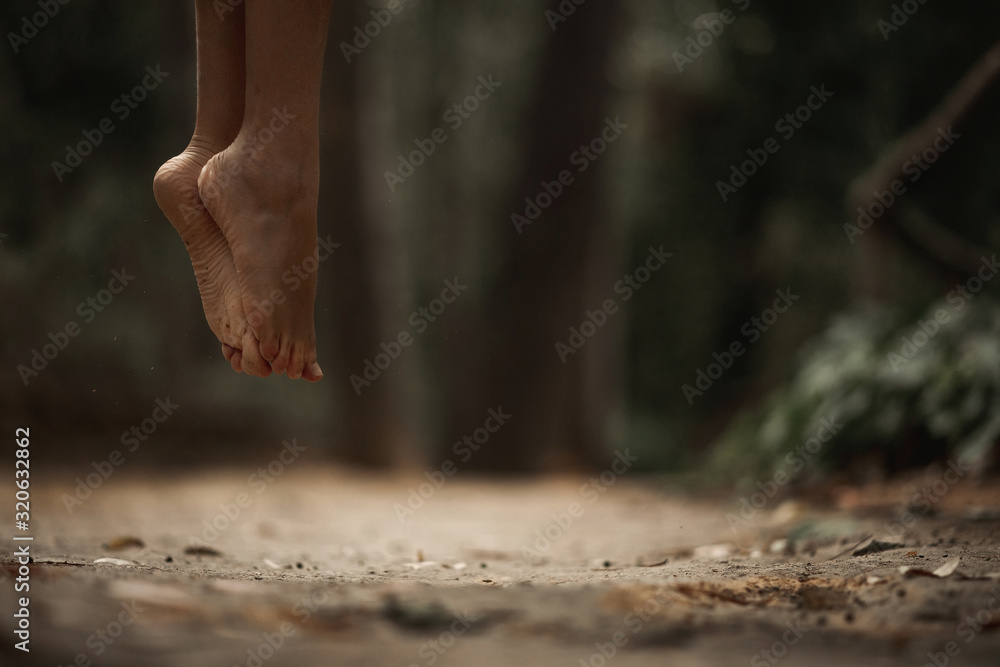 Crop female bare feet jumping above ground in autumnal forest on blurred background Crop female bare feet jumping above ground in autumnal forest on blurred background