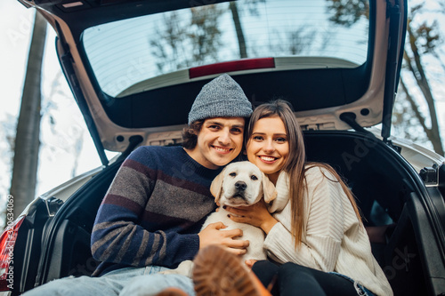 Cute couple have a weekend time with their labrador retriver sitting in automobile in the autumn forest.