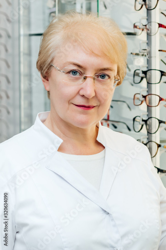 Professional senior female optician offering glasses in optics store