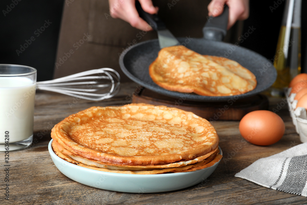 Woman cooking delicious thin pancakes at wooden table Woman cooking delicious thin pancakes at wooden table