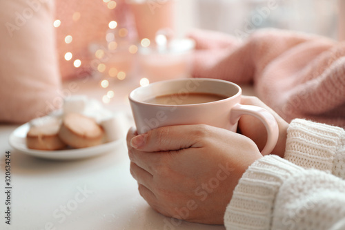 Woman holding cup of delicious hot coffee at white table, closeup. Winter drink