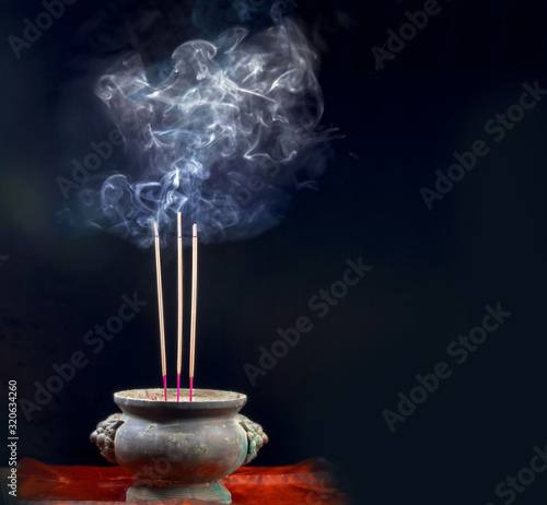 Holder and burning incense sticks with a lot of smoke on dark background