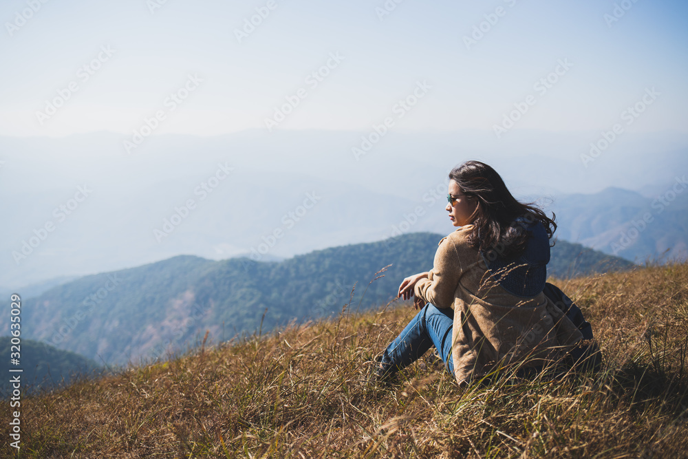 The back view of Asian women traveler wearing sunglasses Sitting on the top of the hill And the golden fields