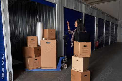 Woman working with a laptop in a moving storage room organizing the boxes in a self storage warehouse