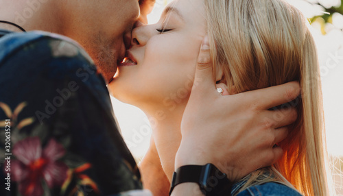 Canvas Print Side view close up portrait of a lovely young couple kissing and smiling while traveling against sunset