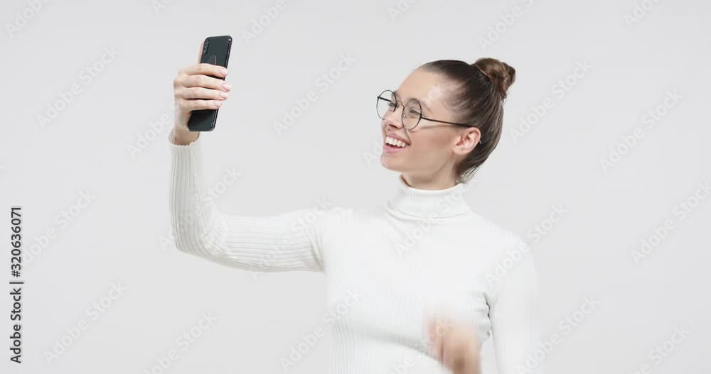 Young European girl talking on the phone with friend, using videochat via smartphone, smiling happily isolated on gray background Young European girl talking on the phone with friend, using videochat via smartphone, smiling happily isolated on gray background