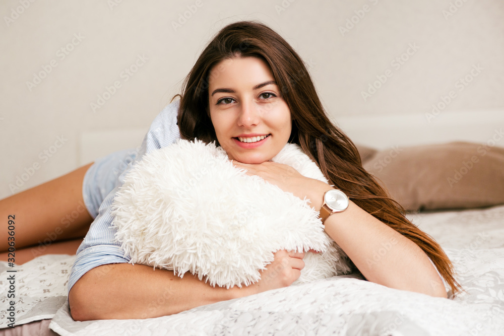 Young smiling woman lying with pillow in bed in her bedroom. Happy morning. Young smiling woman lying with pillow in bed in her bedroom. Happy morning.