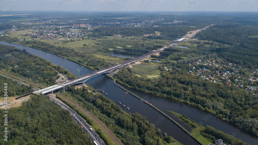 A large and long bridge under construction with cranes across the water from a high hill A large and long bridge under construction with cranes across the water from a high hill