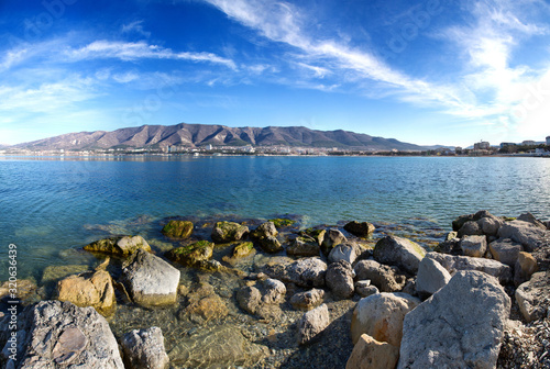 Autumn panorama of Gelendzhik Bay. Clear air, clear sky, and sharp clarity. In the foreground are rocks and a beach. In the background the Caucasus mountains