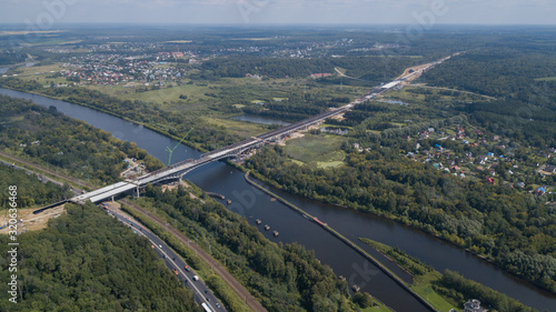 A large and long bridge under construction with cranes across the water from a high hill