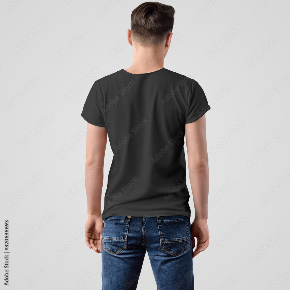 Obraz premium Mockup of a black T-shirt on a young guy in blue jeans, standing back, on a white background.