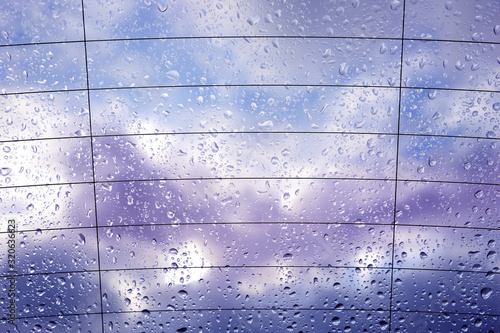 Krople deszczu na tylnej szybie samochodu z chmurami w tle.