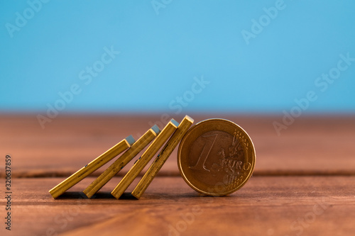 Картината върху платно One euro coin and falling golden domino on a wooden backround