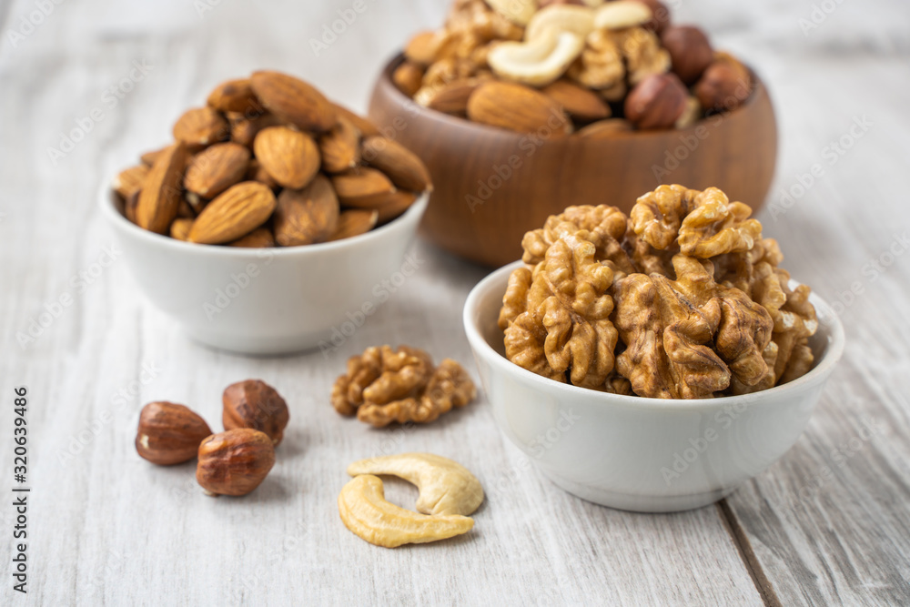 Different nuts in white and wooden bowls on wood table Different nuts in white and wooden bowls on wood table