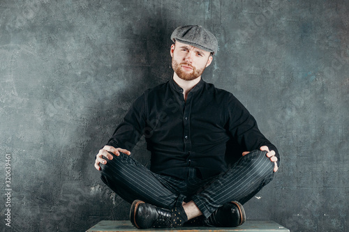 Appeasement. A bearded man in a cap sits in a lotus position on the table. Business concept. Yoga and business