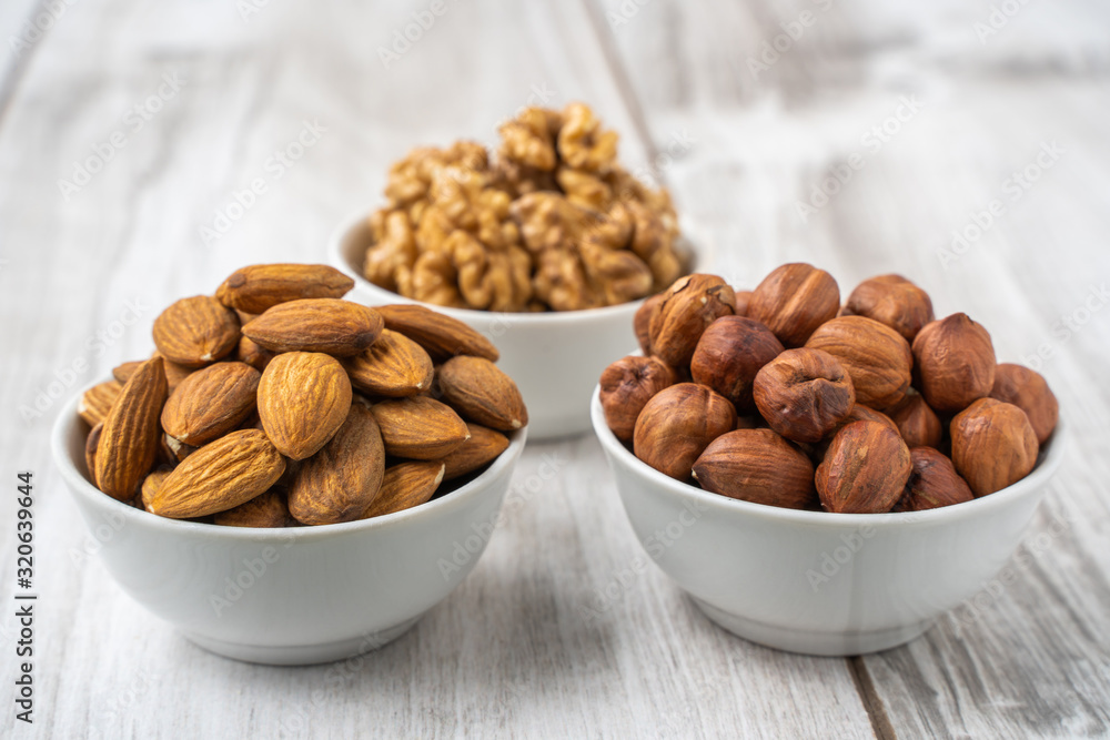 Different nuts in white bowls on wood table Different nuts in white bowls on wood table