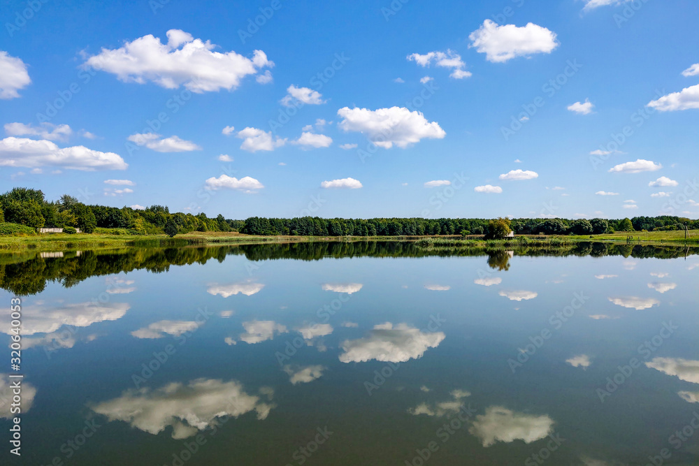Beautiful landscape, reflection in clear water. Lake against the blue sky with white fluffy clouds.