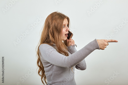 Photography a young beautiful red haired woman in gray sweater is talking on phone gossiping